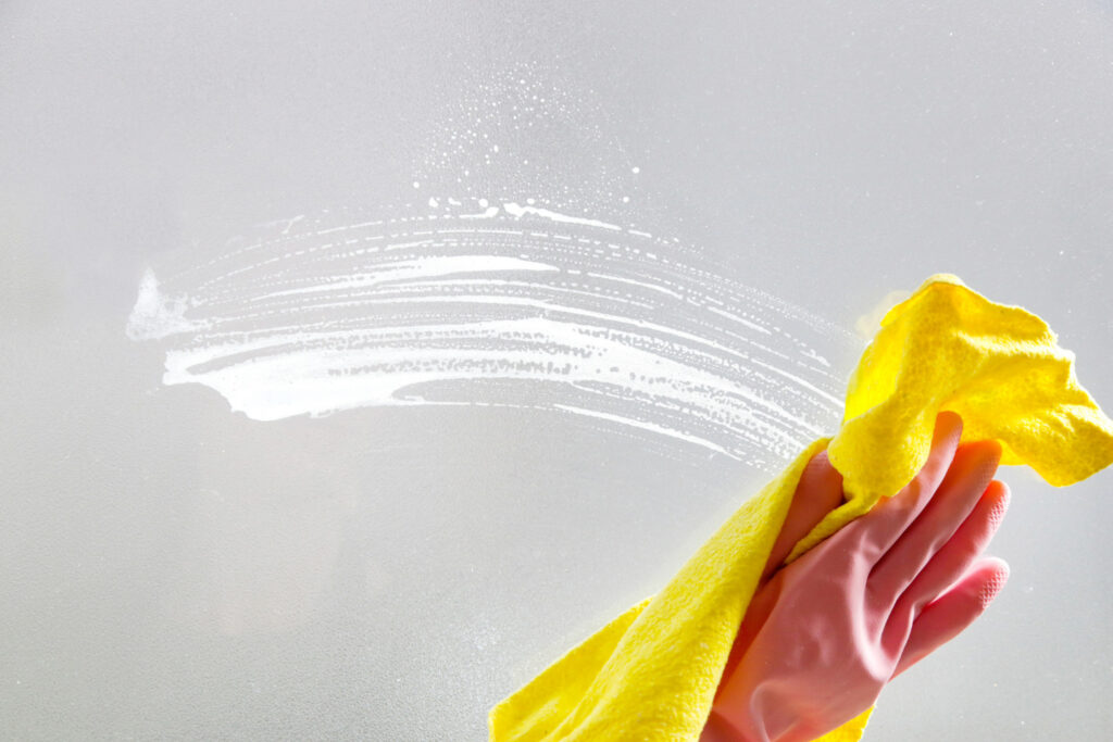 Person med hink och trasa rengör köksfönster en solig dag.